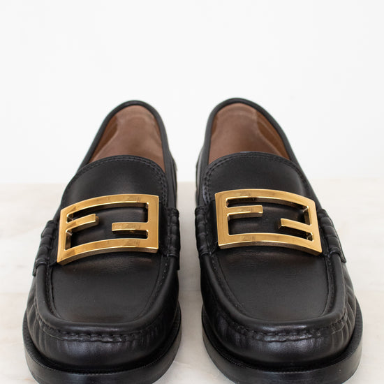 Black loafers with gold buckles on a white background