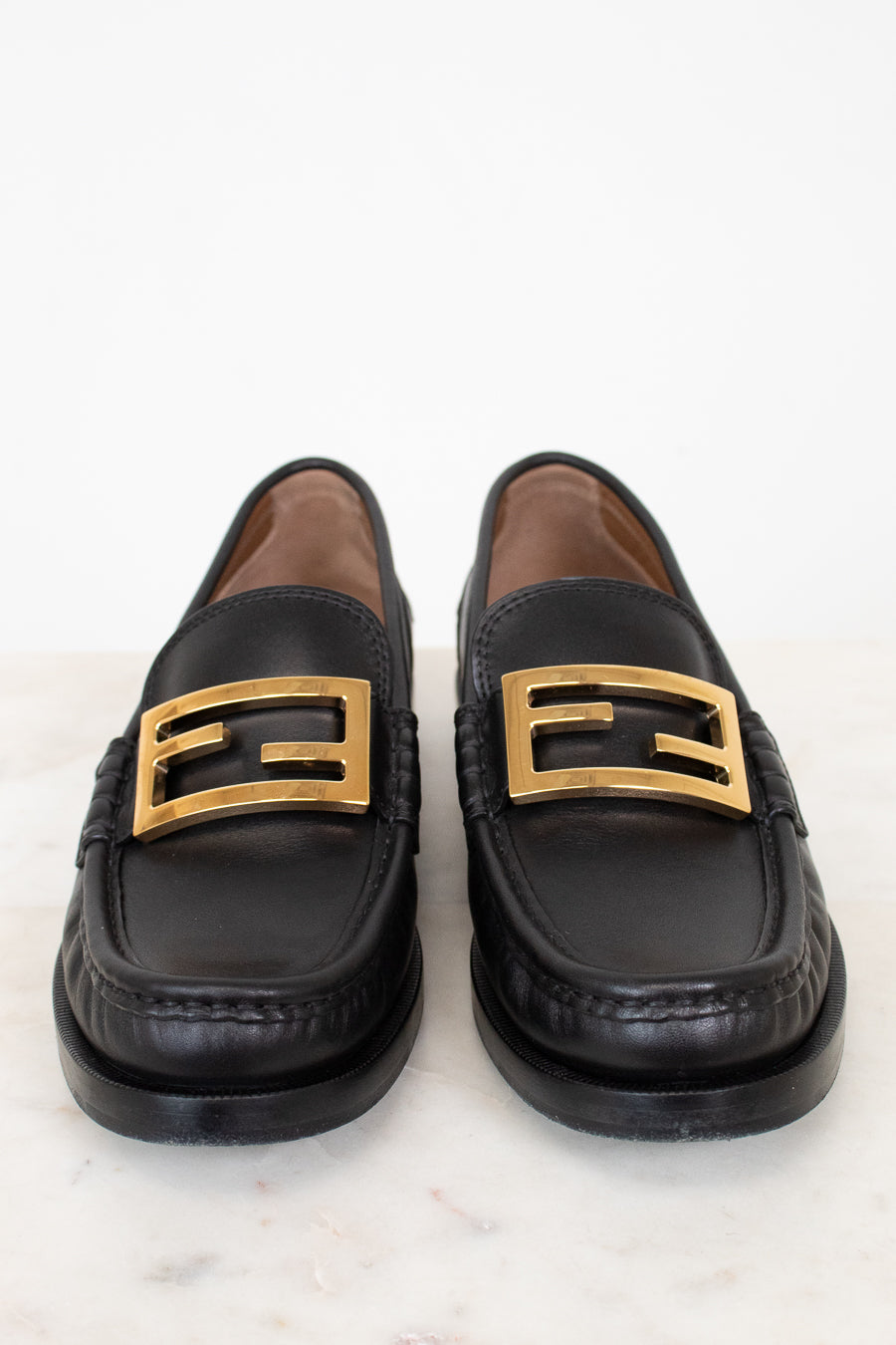 Black loafers with gold buckles on a white background
