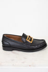 Black loafer with gold buckle on a white marble surface