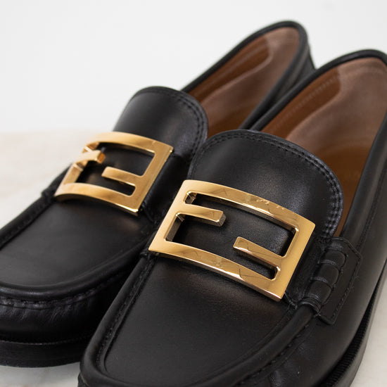 Black loafers with gold buckles on a light background