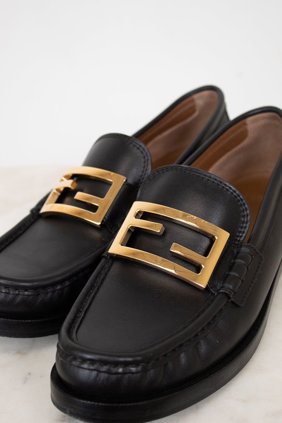Black loafers with gold buckles on a light background