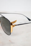 Fendi sunglasses with a black frame, dark lenses, and signature gold metal hardware, resting on a light marble surface.