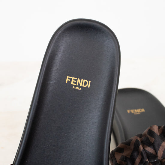 Black Fendi sandals with gold logo on a light background