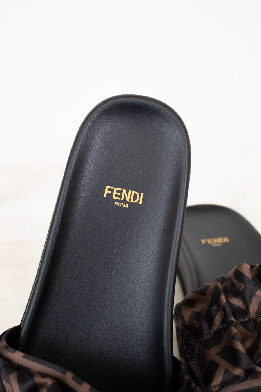 Black Fendi sandals with gold logo on a light background