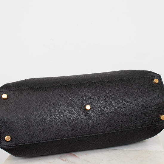 Black leather handbag with gold studs on bottom of bag sitting on a light gray background