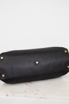 Black leather handbag with gold studs on bottom of bag sitting on a light gray background