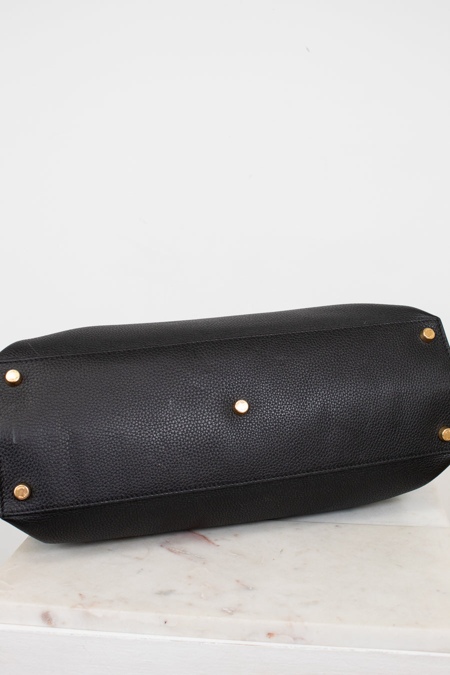 Black leather handbag with gold studs on bottom of bag sitting on a light gray background