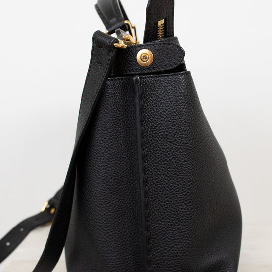 Black leather handbag with gold zipper on a light gray background