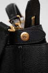 Close-up of a black leather bag with gold hardware on a light gray background