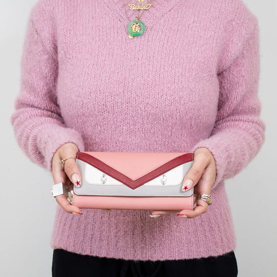 Person wearing a pink sweater holding a pink and white and pink clutch against a plain background