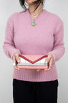 Person wearing a pink sweater holding a pink and white and pink clutch against a plain background