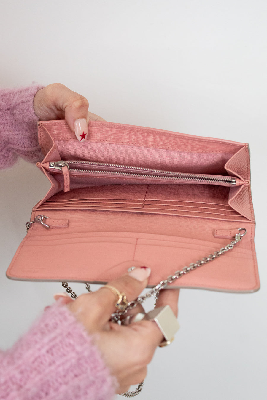 Pink wallet held open by a hand against a light background