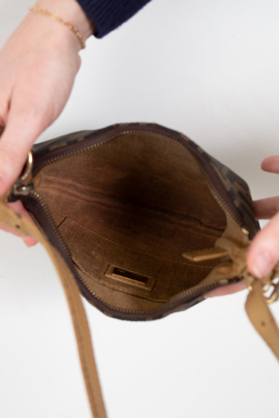 Brown handbag with a strap held open by hands on a white background
