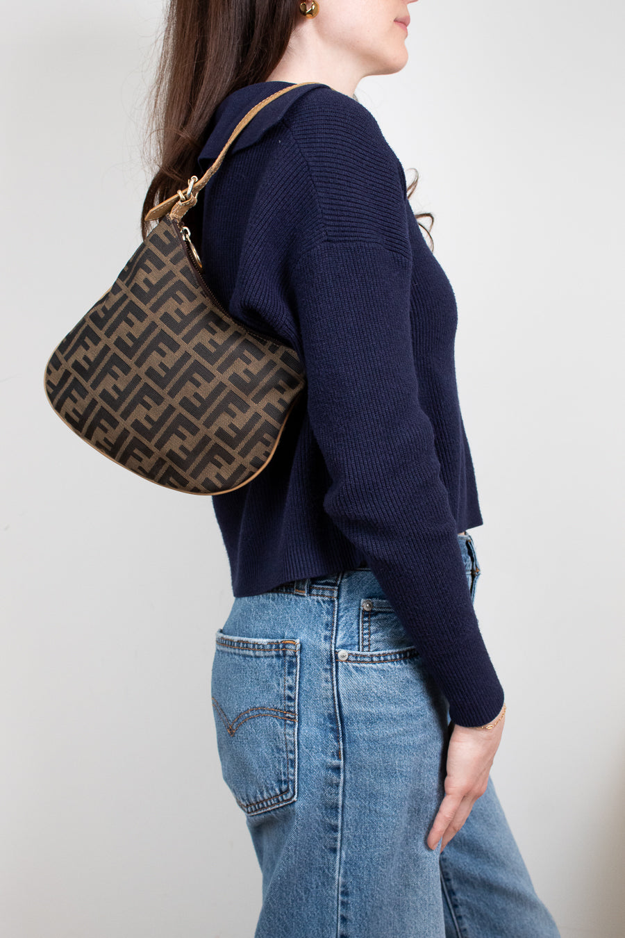 Person wearing a navy sweater and blue jeans, holding a patterned handbag.