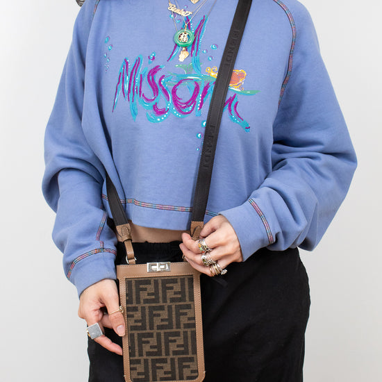 Person wearing a blue sweatshirt with colorful text and graphics, holding a patterned phone holder.