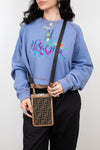 Person wearing a blue sweatshirt with colorful text and graphics, holding a patterned phone holder.