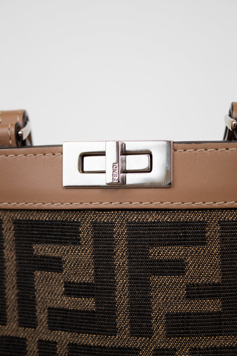 Close-up of a brown phone holder with a silver clasp and decorative logos on a light gray background