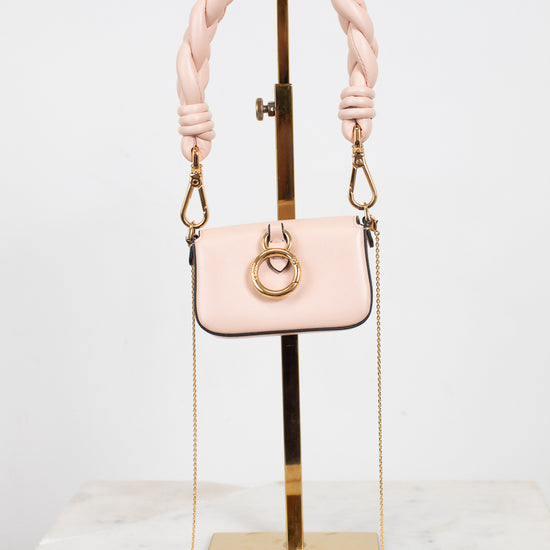 A small blush pink handbag with a thick braided shoulder strap and gold-tone hardware, displayed on a gold stand against a white studio background.