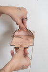 A close-up of a person's hands holding open a small structured light pink leather handbag with gold-tone hardware and a gold chain strap against a plain light background.