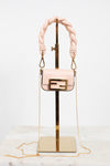 A light pink leather handbag with a gold-tone Fendi double-F logo buckle and a thick braided top handle, displayed on a gold stand against a white background.