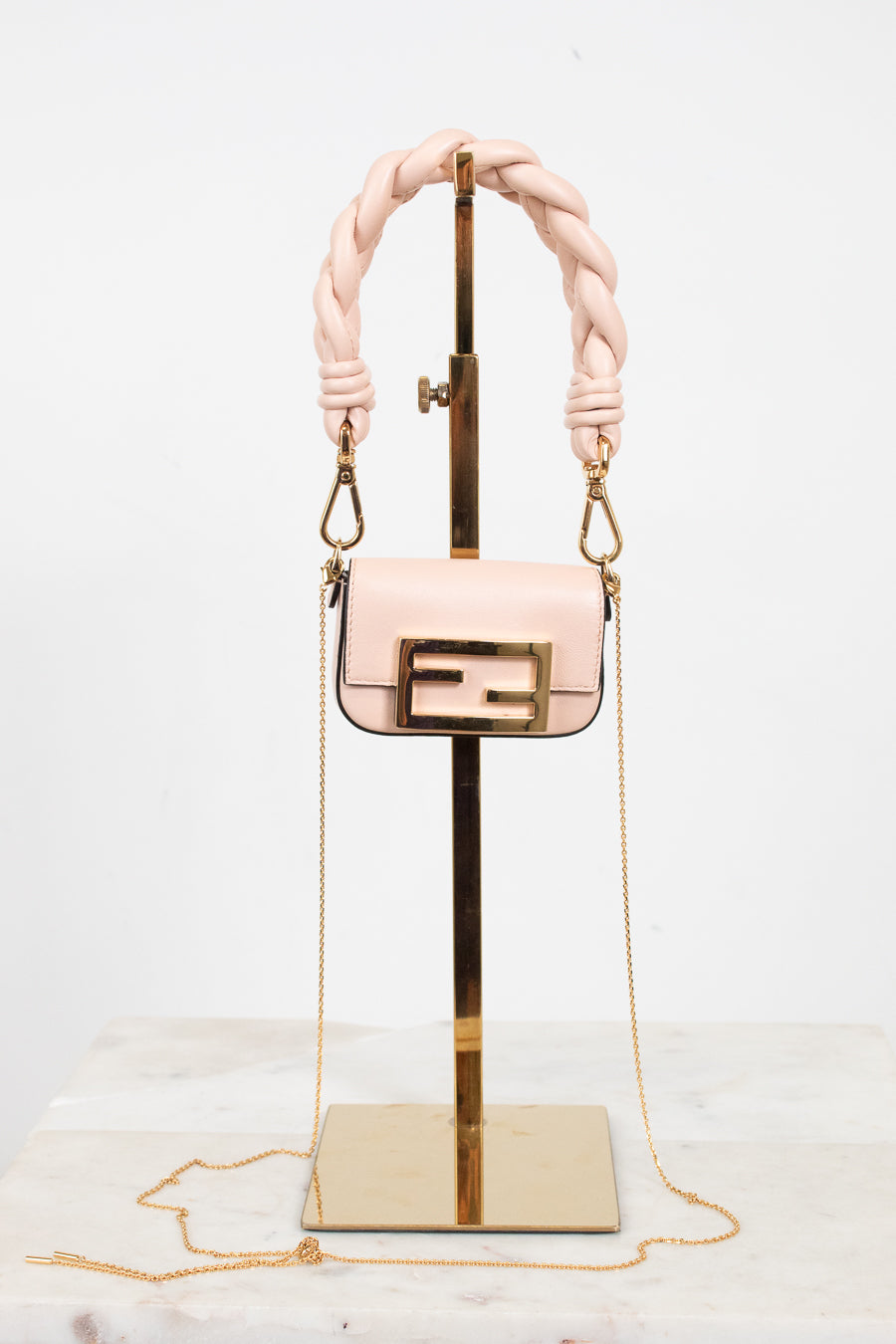 A light pink leather handbag with a gold-tone Fendi double-F logo buckle and a thick braided top handle, displayed on a gold stand against a white background.