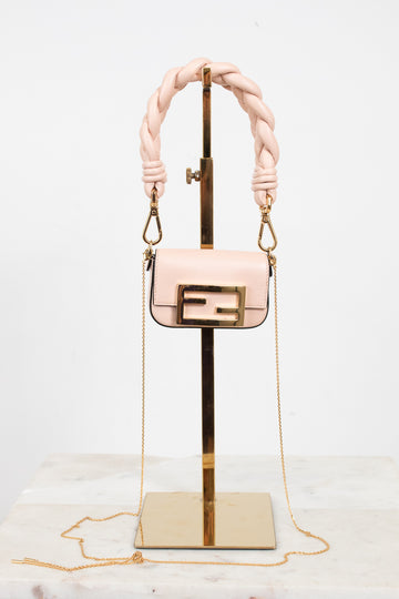 A light pink leather handbag with a gold-tone Fendi double-F logo buckle and a thick braided top handle, displayed on a gold stand against a white background.