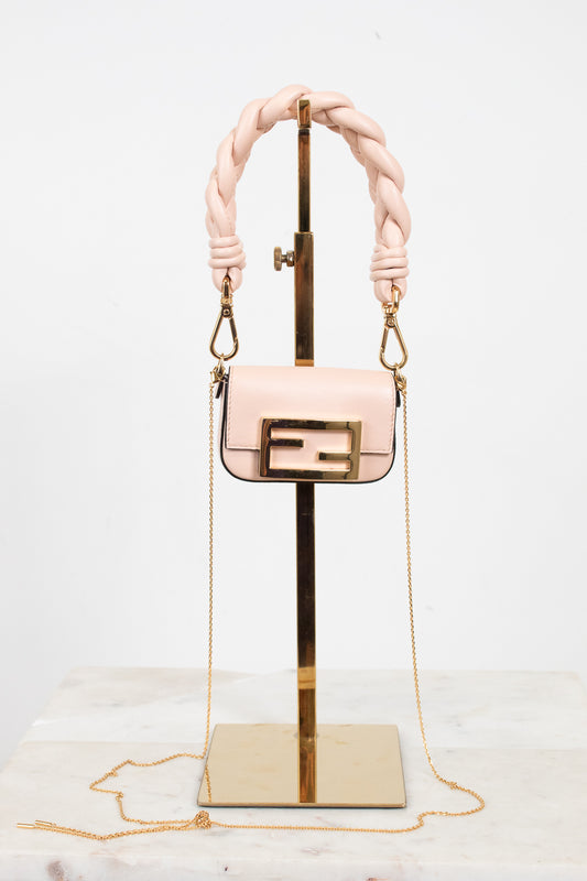 A light pink leather handbag with a gold-tone Fendi double-F logo buckle and a thick braided top handle, displayed on a gold stand against a white background.