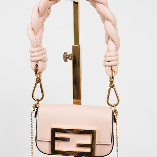 A light pink leather handbag with a gold-tone FF logo clasp and a thick braided shoulder strap, displayed on a gold stand against a white background.