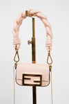 A light pink leather handbag with a gold-tone FF logo clasp and a thick braided shoulder strap, displayed on a gold stand against a white background.