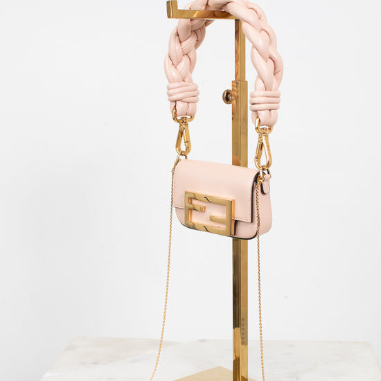 A light pink leather shoulder bag with a chunky braided shoulder strap and gold-tone hardware, displayed on a gold metal stand against a white background.