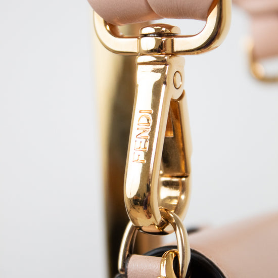Close-up of a Fendi handbag strap in blush pink leather with a polished gold-tone metal clasp engraved with the Fendi logo.