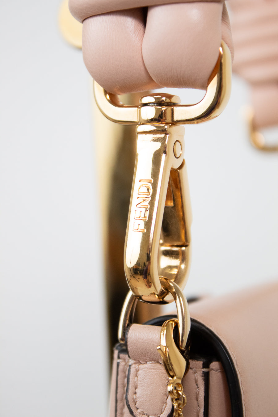 Close-up of a Fendi handbag strap in blush pink leather with a polished gold-tone metal clasp engraved with the Fendi logo.