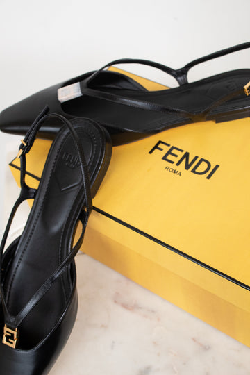 Black Fendi strappy flat shoes displayed next to a bright yellow Fendi box on a light marble surface.