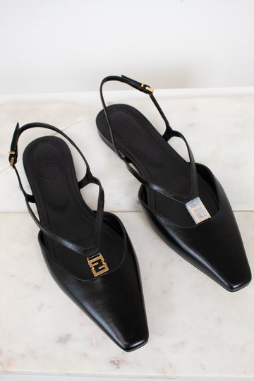 A pair of black leather pointed-toe slingback flats with gold-tone Fendi FF logo hardware, displayed on a light marble surface.