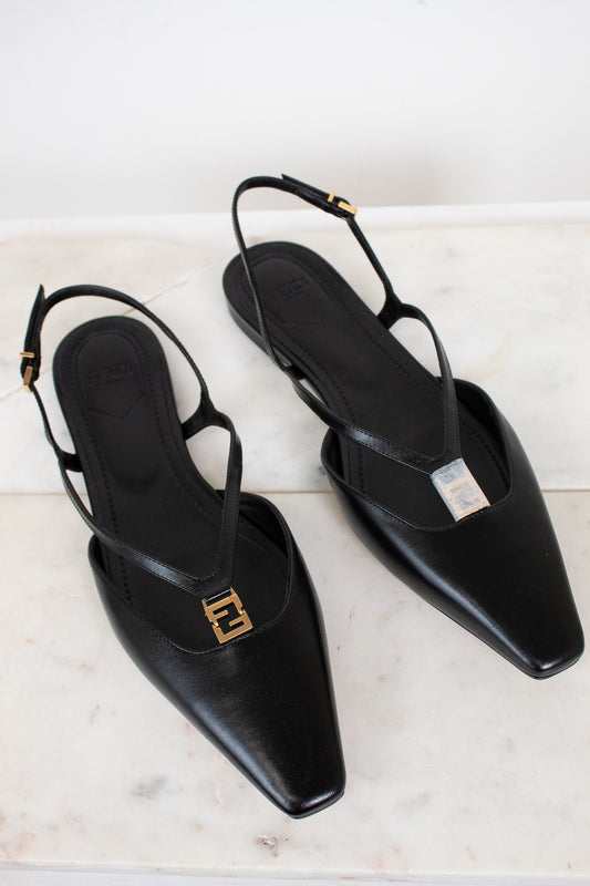 A pair of black leather pointed-toe slingback flats with gold-tone Fendi FF logo hardware, displayed on a light marble surface.