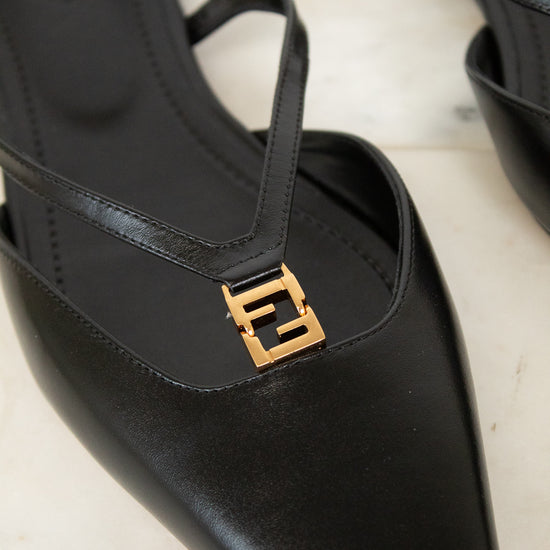 A close-up of a black leather pointed-toe slingback shoe with a gold-tone interlocking FF logo hardware on the strap, resting on a light marble surface.