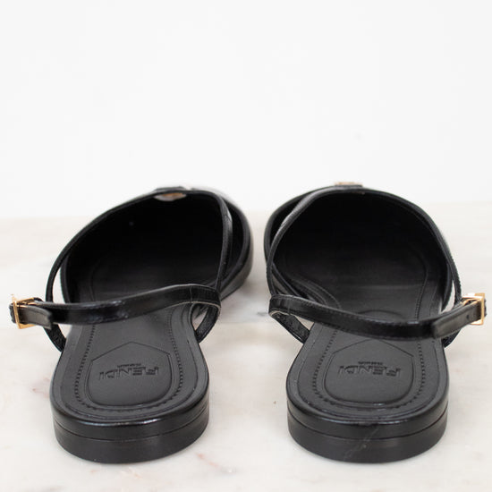 A pair of black Fendi slingback flat sandals with gold-tone buckle details, shown from the back on a white marble surface against a white background.