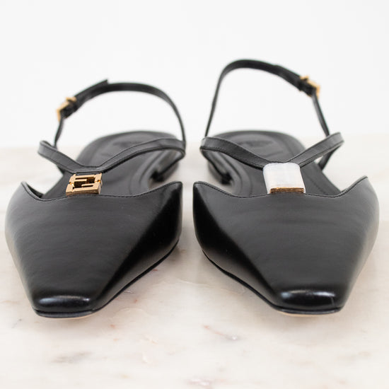 A pair of black leather pointed-toe slingback flats with gold-tone Fendi logo hardware, displayed on a white marble surface against a white background.