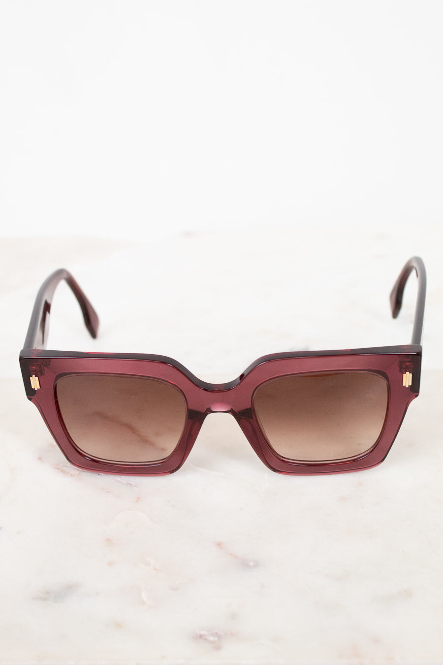 Sunglasses with a purple tinted frame and brown gradient lenses on a light background