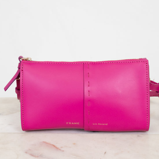 Pink crossbody bag with Frame/Les Second brand name on a light marble background