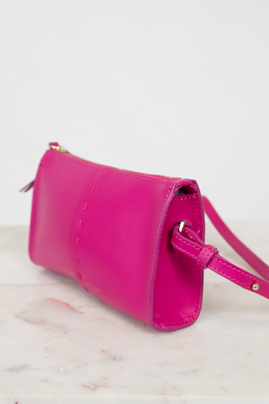 Pink crossbody bag on a light marble surface with a white background