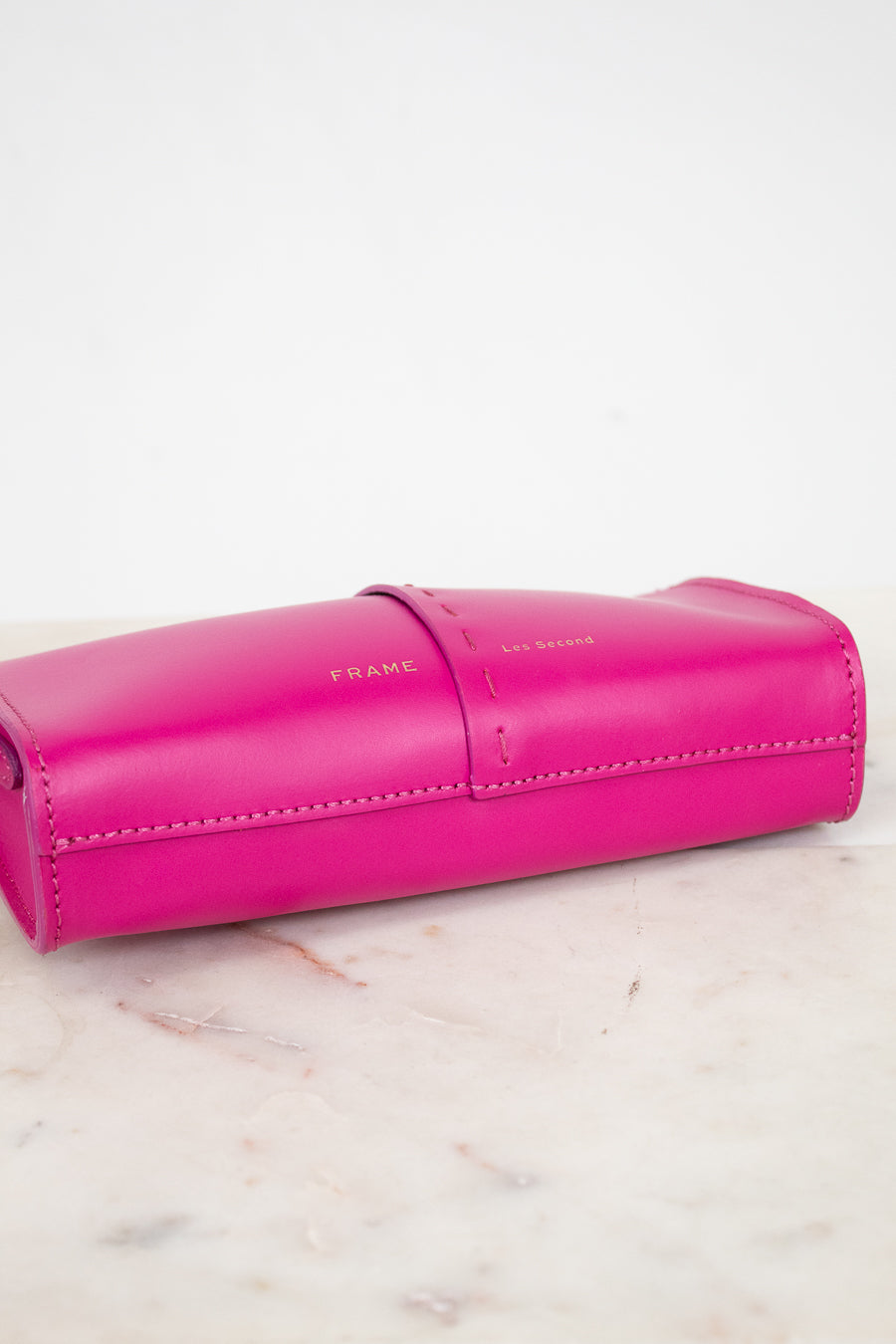 Pink crossbody bag with Frame/Les Second brand name on a light marble 