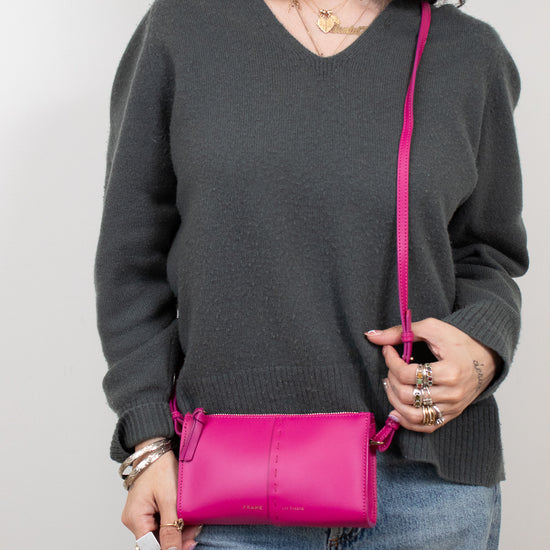 Person wearing a gray sweater holding a pink crossbody bag against a plain background