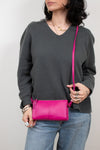 Person wearing a gray sweater holding a pink crossbody bag against a plain background