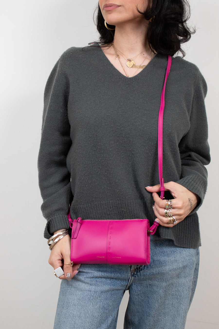 Person wearing a gray sweater holding a pink crossbody bag against a plain background