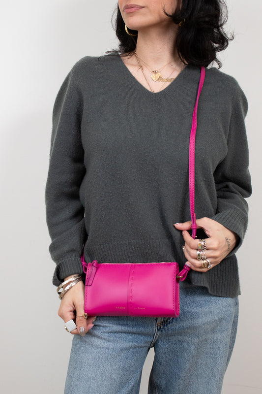 Person wearing a gray sweater holding a pink crossbody bag against a plain background