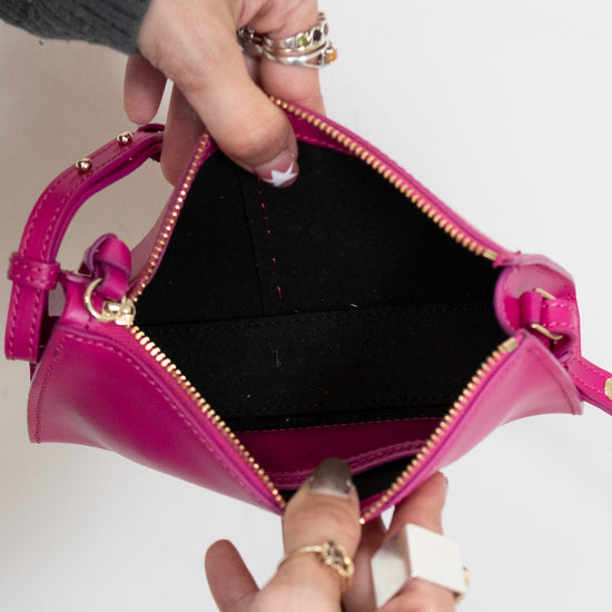 Person holding a pink handbag open with black interior showing with a plain background