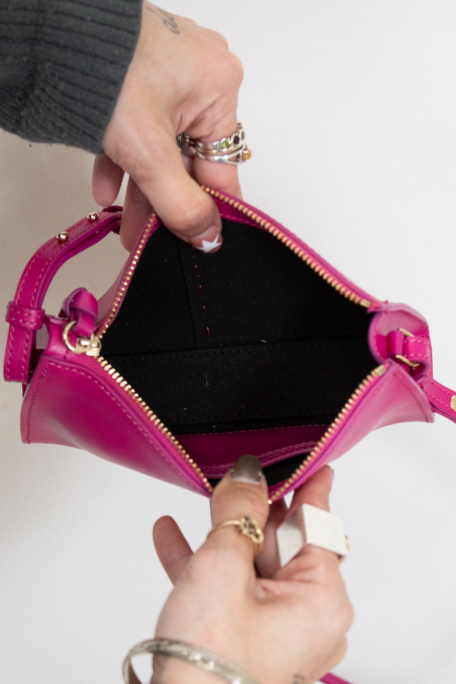 Person holding a pink handbag open with black interior showing with a plain background