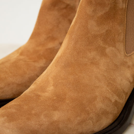 Close-up of a tan suede ankle boot with a dark sole, showing the side elastic gore and textured suede upper.
