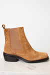 A tan suede Chelsea boot with a brown elastic side panel and a dark brown block heel, shown from a side profile on a light marble surface against a white background.